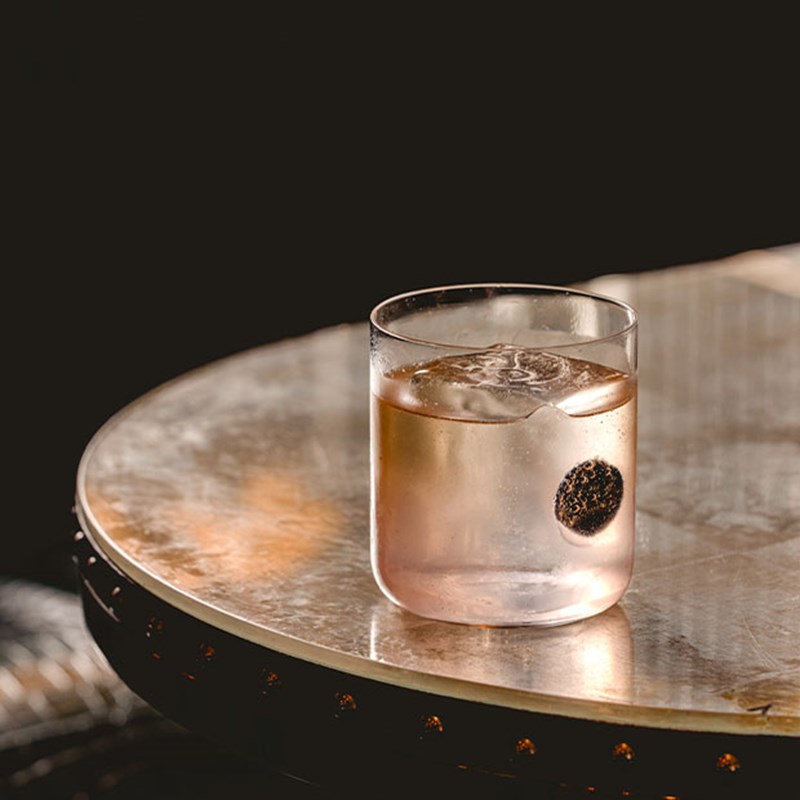 A sophisticated cocktail in a delicate glass with a vibrant red garnish, set against a moody, elegant backdrop.